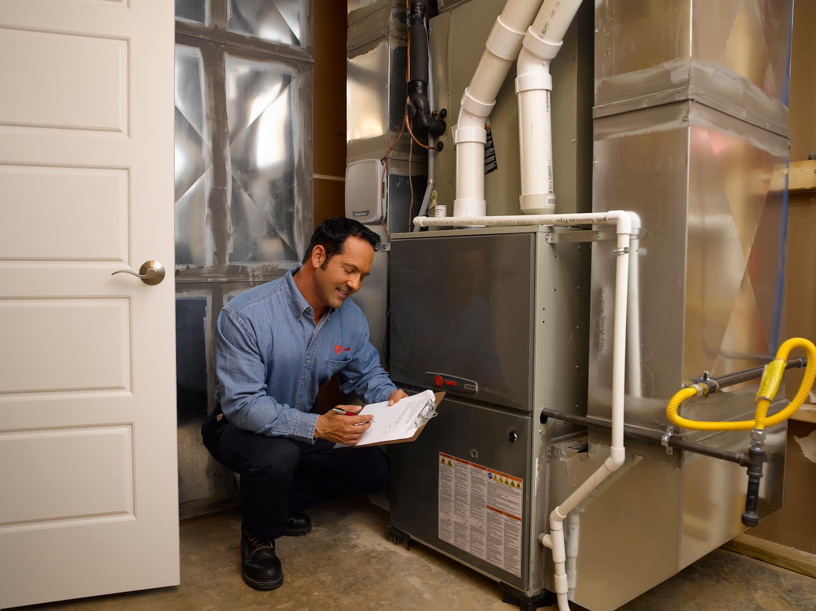 HVAC technician in a denim Trane shirt smiles while inspecting an indoor Trane HVAC system.