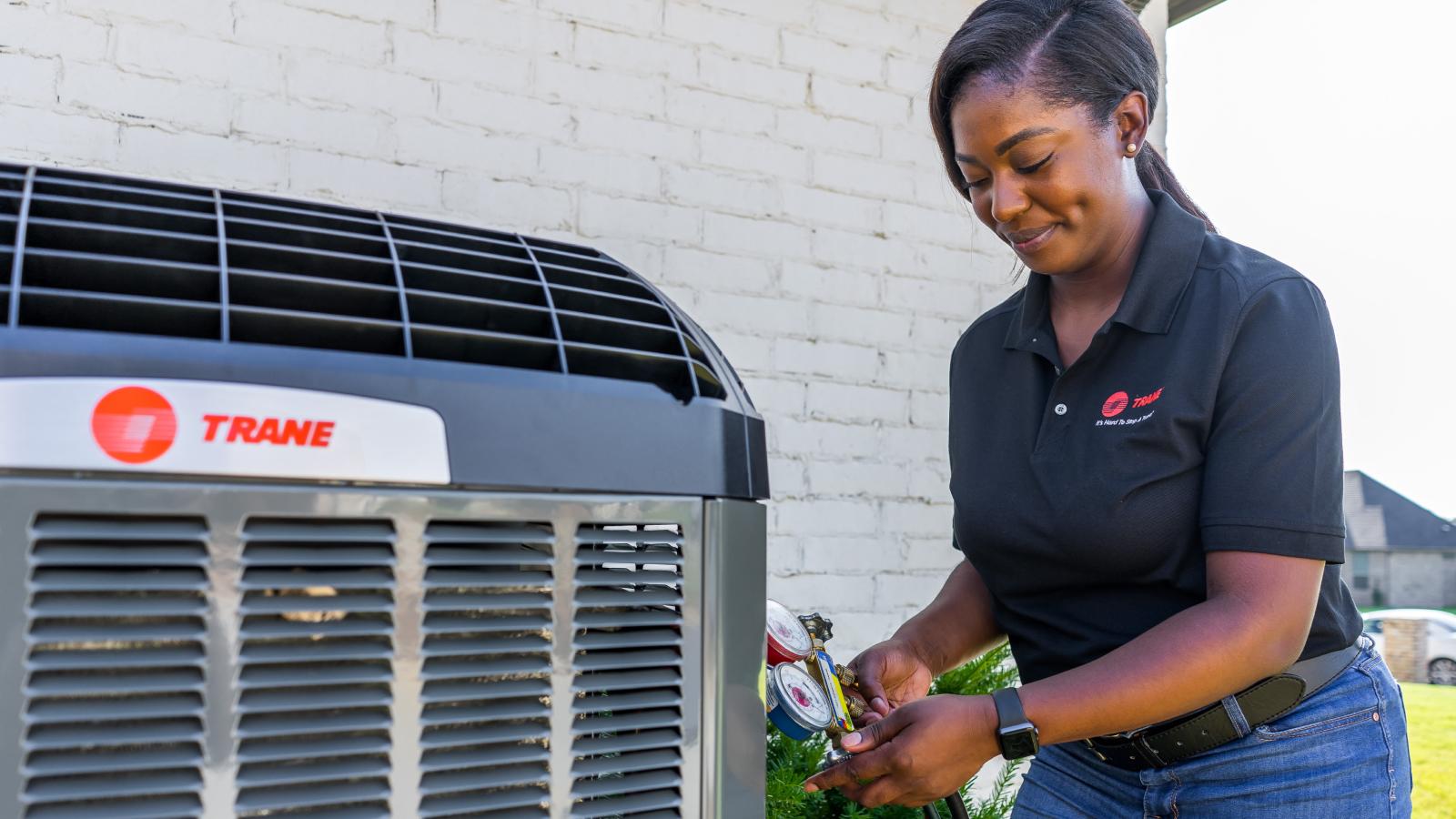 An HVAC dealer with a Trane logoed t-shirt inspects an outdoor Trane system.