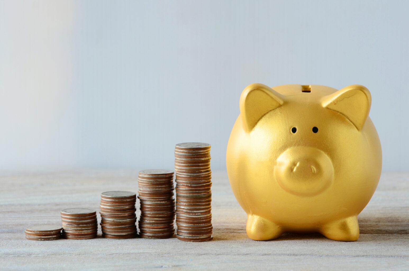 Yellow piggy bank sits next to one tall and one short stack of quarters.
