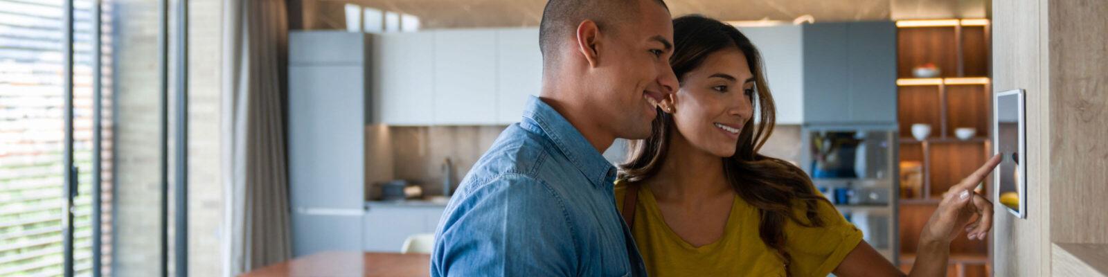 A couple setting their touch-screen enabled smart thermostat.