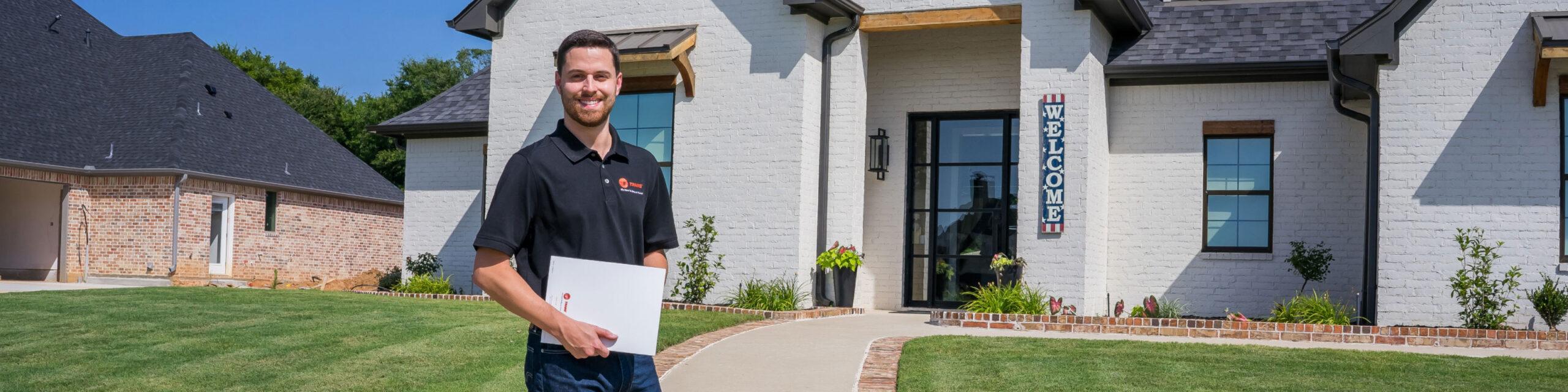 Young white male HVAC worker is standing in front of a white house.