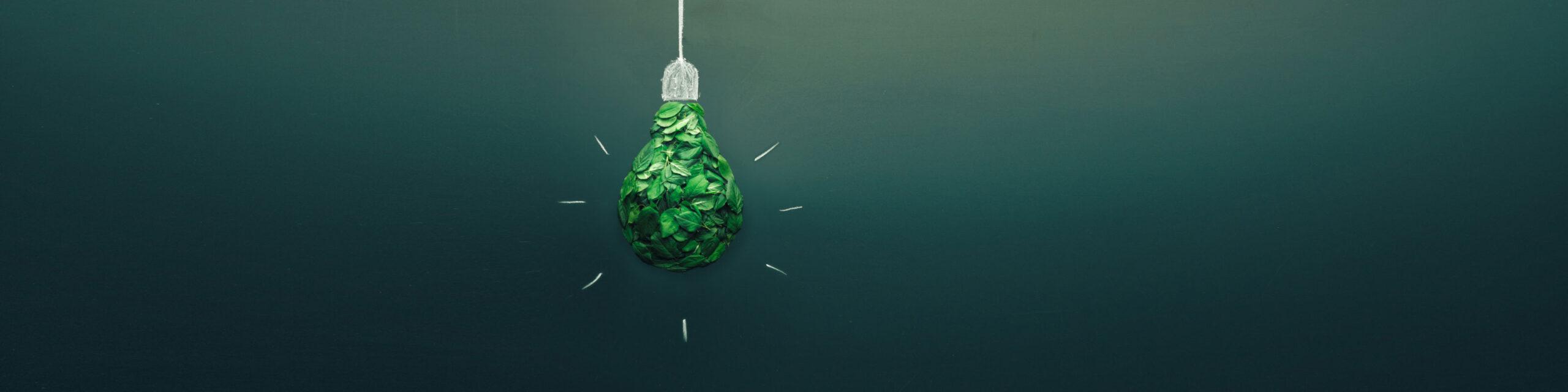 A green paper light bulb sculpture hangs in front of a dark green wall.