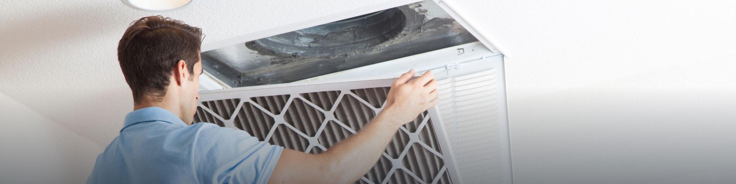 A young caucasian man in a blue shirt is changing a home air filter.