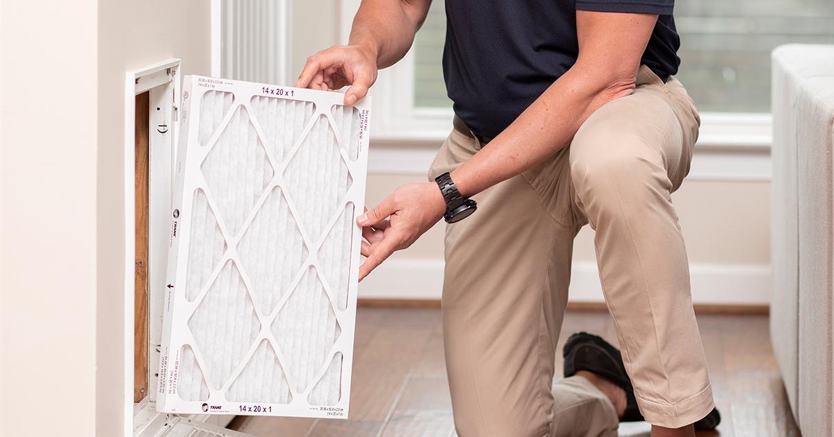 A Trane HVAC technician is replacing an air filter.