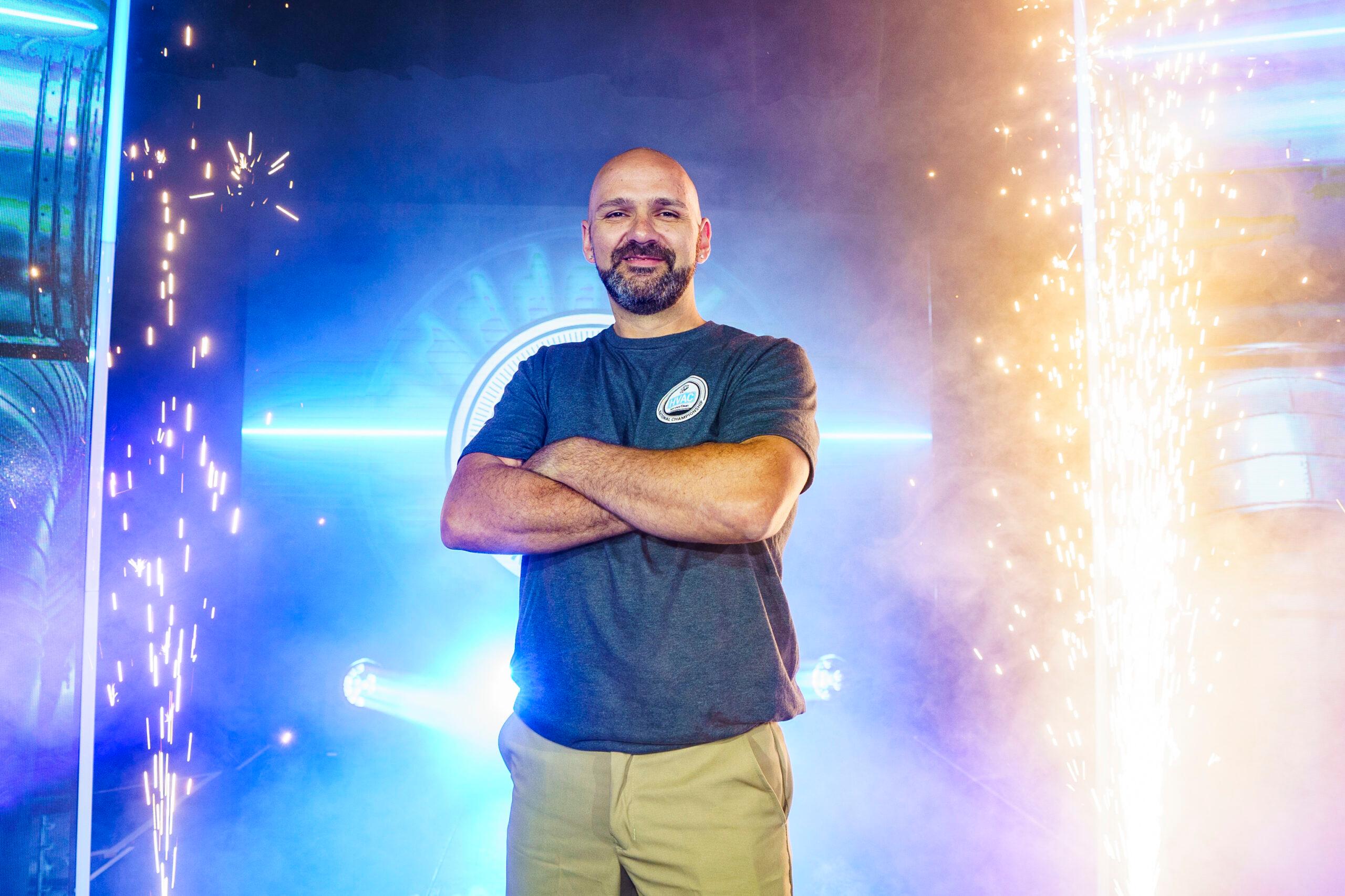 A man stands smiling with his arms crossed on a stage.